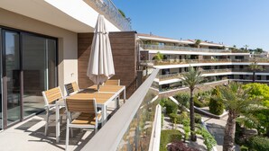 A balcony with a table and chairs, a glass railing, and a view of other buildings and greenery. - Apartment 'T2 Muses' with Private Terrace, Wi-Fi and Air Conditioning (Le Crès)