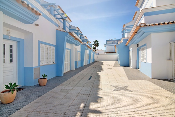 A narrow street lined with buildings featuring blue and white facades, potted plants, and a star-shaped pavement design.