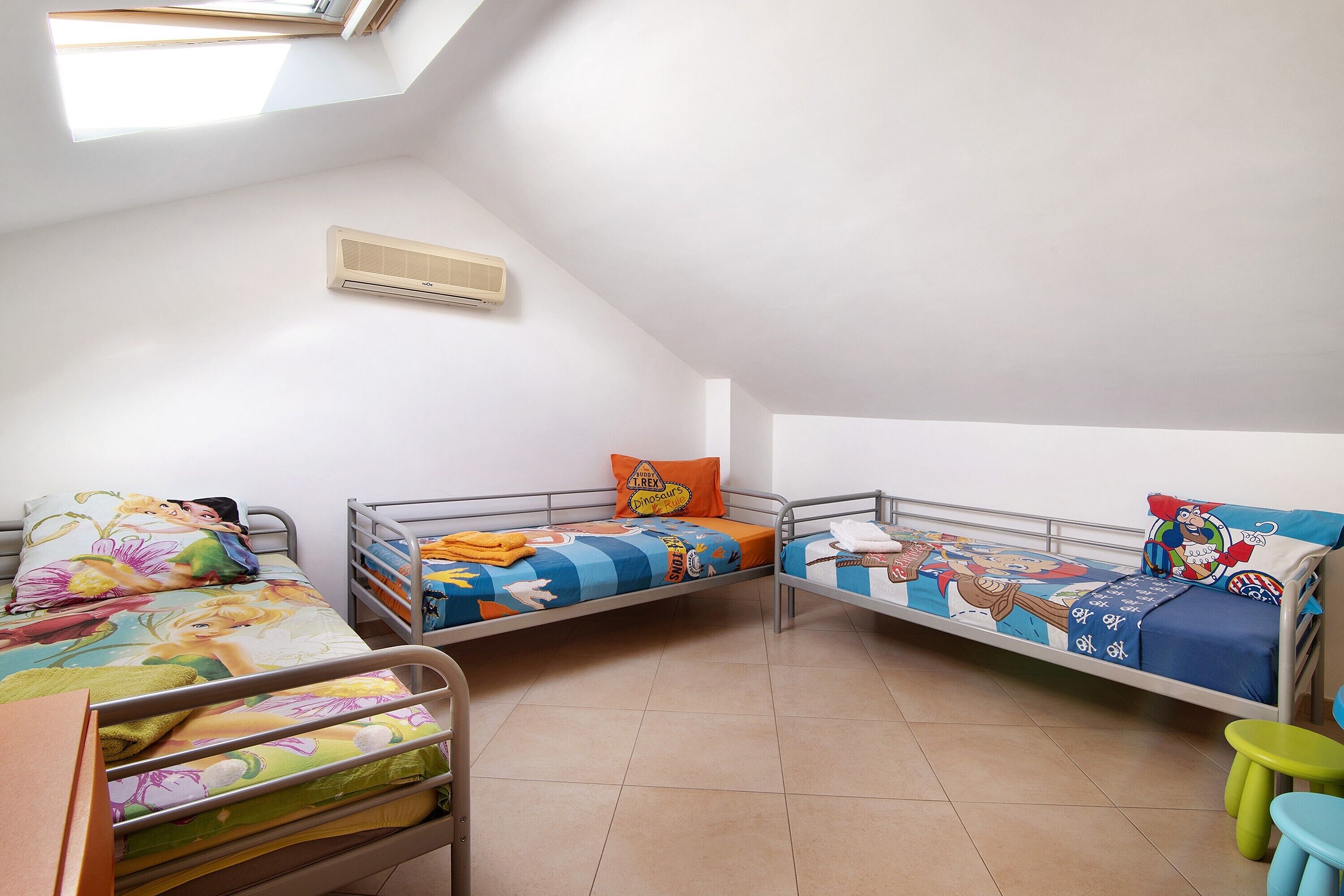 Un dormitorio con tres literas, una ventana, un radiador y un taburete pequeño.
