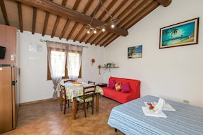 Ein Zimmer mit einem Bett, einem Esstisch mit Stühlen, einem roten Sofa, einem Fernseher und einer Holzbalkendecke.