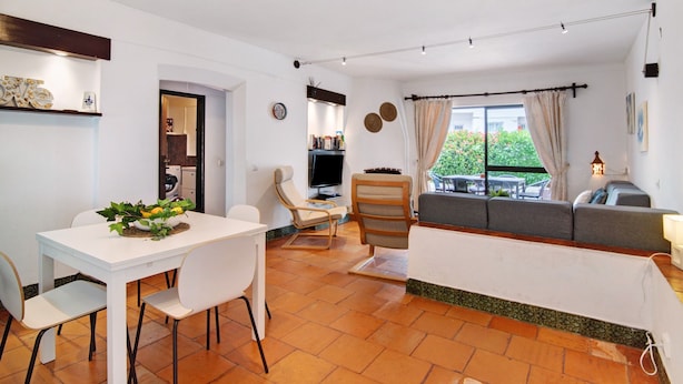 Una sala de estar moderna con un sofá, una mesa de comedor con sillas, un televisor y una ventana con cortinas.