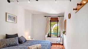 Un dormitorio con cama, ventana con cortinas, una silla y perchero de pared.