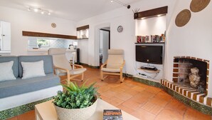 Sala de estar con sofá, sillas, televisor, chimenea y zona de cocina al fondo.