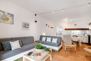 Een moderne woonkamer met een grijze bank, een salontafel met een plant en een eethoek met stoelen en een tafel.