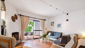 Una sala de estar con un sofá, dos sillones, una mesa de centro, una chimenea y una zona de comedor con mesa y sillas.