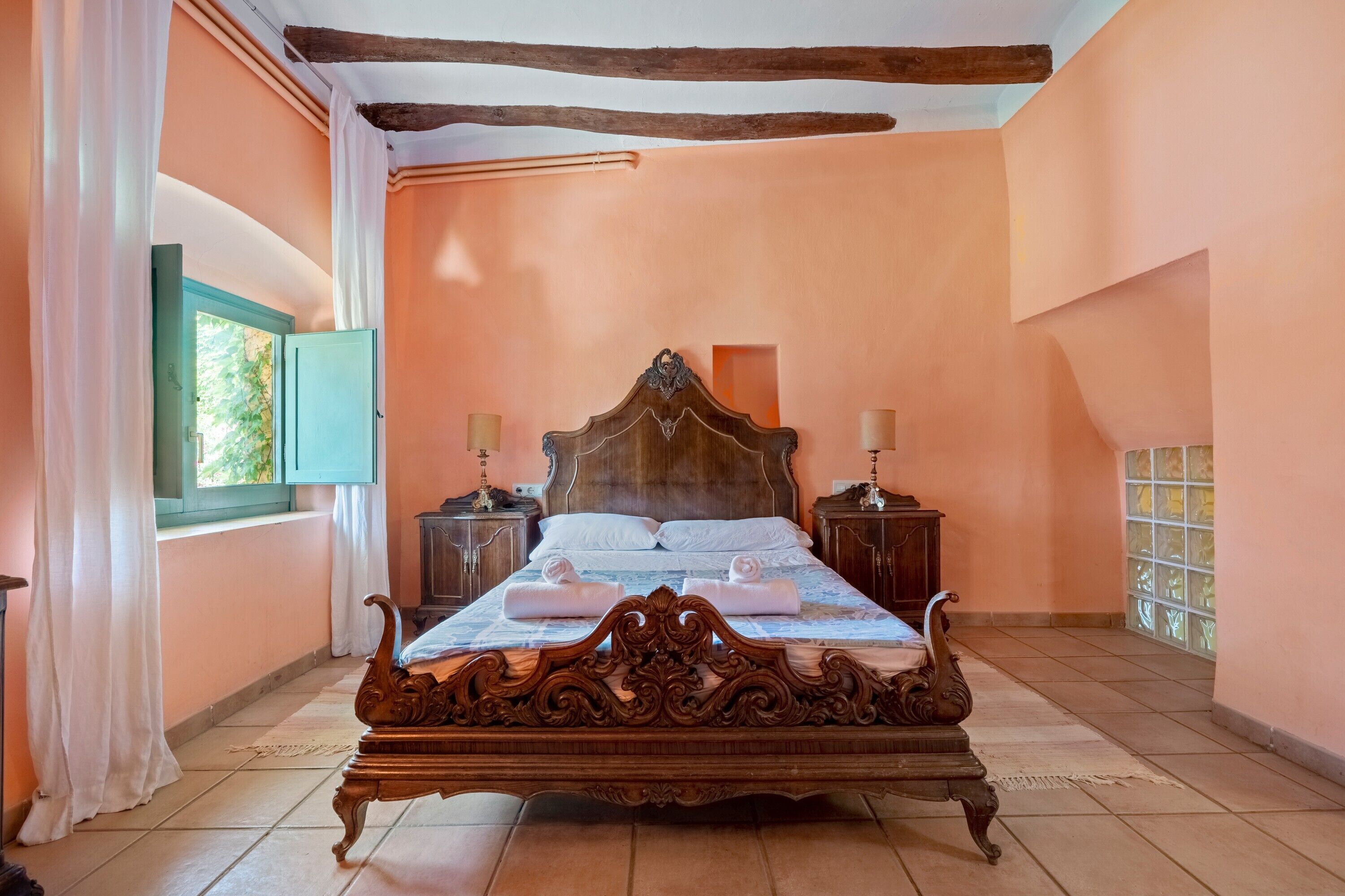 Une chambre à coucher avec un lit en bois, deux tables de chevet, une fenêtre avec des rideaux et une vue sur la verdure.