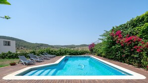 Ein rechteckiger Pool mit Holzterrasse, umgeben von Liegestühlen und blühenden Büschen.