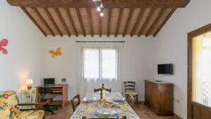 A dining area with a table set for four, a sofa, a TV, and a wooden cabinet. - Farmhouse "Il Pino - Mandorlo" with Shared Pool, Private Terrace & Wi-Fi (Cecina)