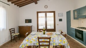 A dining area with a table set for four, a wooden cabinet, a television, and a kitchen with blue cabinets and a gas stove. - Farmhouse "Il Pino - Mandorlo" with Shared Pool, Private Terrace & Wi-Fi (Cecina)