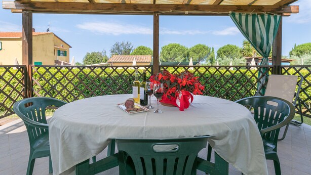 A covered outdoor patio with a round table, chairs, a tablecloth, wine bottles, and a bouquet of flowers. - Farmhouse "Il Pino - Mandorlo" with Shared Pool, Private Terrace & Wi-Fi (Cecina)