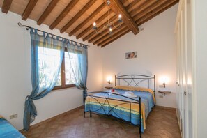 Een slaapkamer met een bed, gordijnen, een kroonluchter, een nachtkastje en een wandplank.