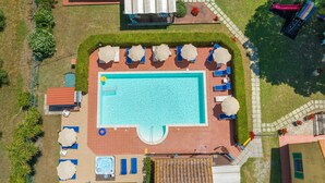Eine Vogelperspektive auf einen Poolbereich mit Liegestühlen, einem Whirlpool und einer überdachten Terrasse.