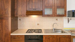 A kitchen with wooden cabinets, a gas stove, a sink, and a microwave. - Farmhouse "Il Pino - Tiglio" with Shared Pool, Private Terrace & Wi-Fi (Cecina)