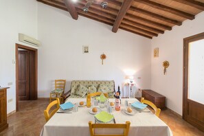 A dining room with a wooden ceiling, a table set for four, and a floral-patterned sofa. - Farmhouse "Il Pino - Tiglio" with Shared Pool, Private Terrace & Wi-Fi (Cecina)