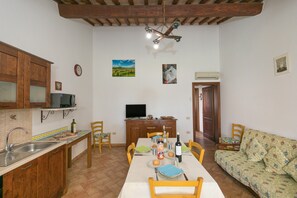 A dining area with a table set for four, a kitchen with wooden cabinets, a television, and a sofa. - Farmhouse "Il Pino - Tiglio" with Shared Pool, Private Terrace & Wi-Fi (Cecina)