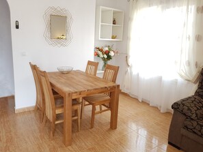 A dining area with a wooden table, chairs, a decorative mirror, and a vase with flowers.