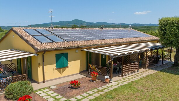 Een geel gebouw met een dakbedekt met zonnepanelen, een overdekte patio en een tuin vol rode bloemen.