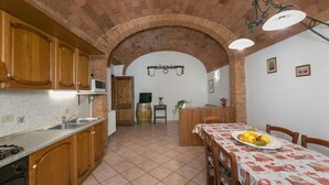 A kitchen with wooden cabinets, a tiled floor, a dining table with a fruit plate, and a brick archway.