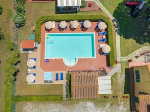 An aerial view of a swimming pool area with lounge chairs, a hot tub, and a covered patio.