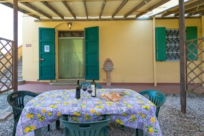 Une terrasse extérieure avec une table dressée pour deux personnes, recouverte d’une nappe à motifs de citron, deux bouteilles de vin et une miche de pain.