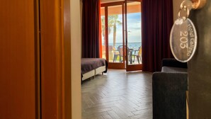 Une chambre d’hôtel avec un lit, un canapé, un balcon donnant sur la mer et un porte-clés portant le nom de l’hôtel.
