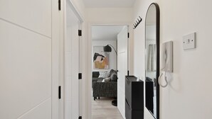 A hallway with a black refrigerator, a large mirror, and a telephone on the wall. - Tropical Inspired 2-Bedroom Flat (Dunmow)