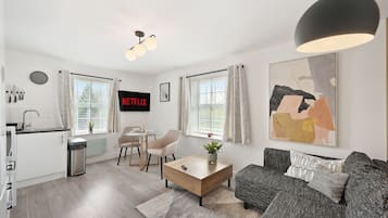 Ein modernes Wohnzimmer mit Sofa, Couchtisch und Kunstwerken. Es gibt eine Küchenzeile mit Spüle und Schränken.