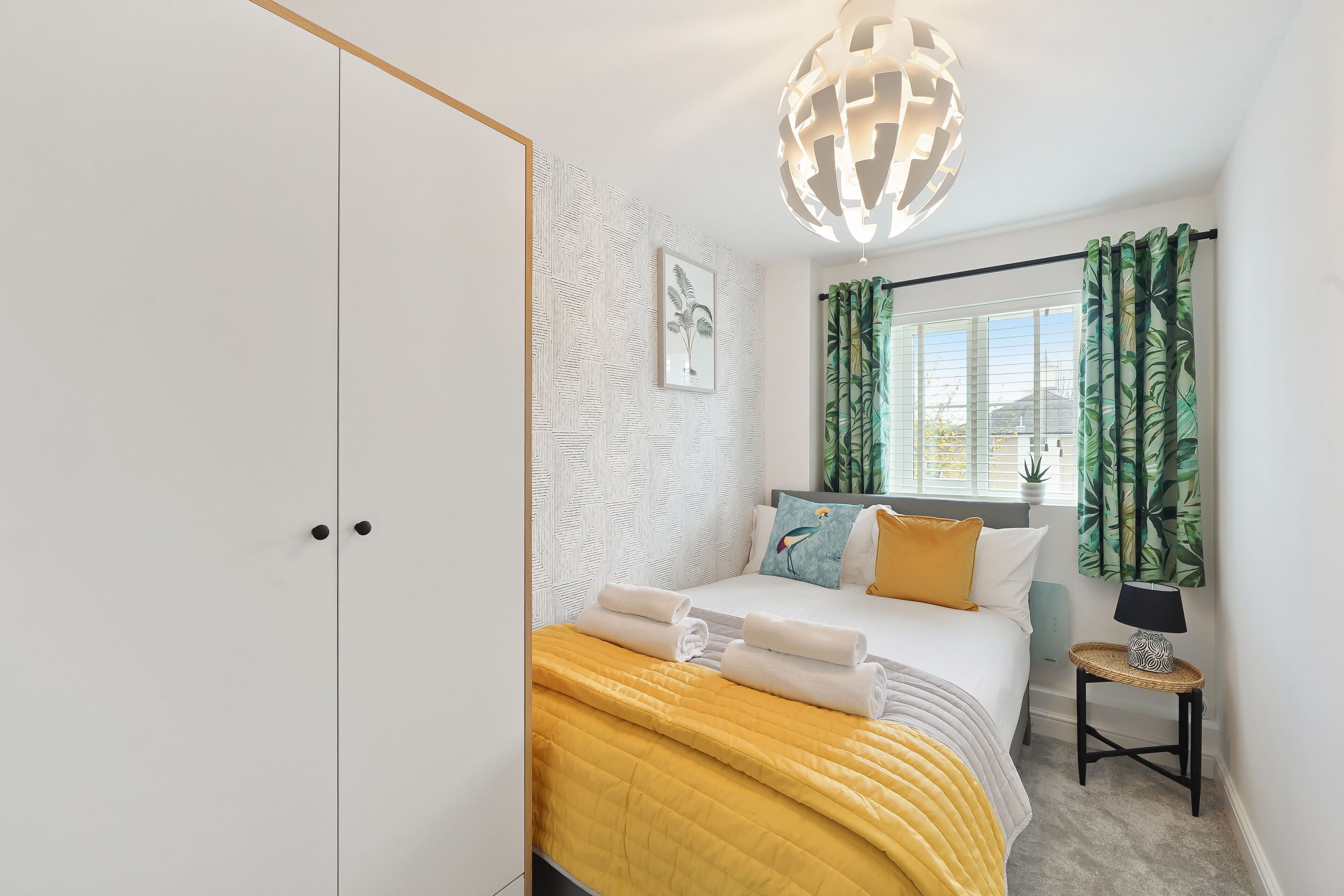 Een slaapkamer met een bed, een nachtkastje met een lamp, een raam met gordijnen en een muur met een structuur.