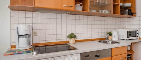 Una cocina compacta con horno integrado, microondas, cafetera y lavabo.