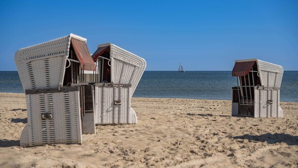 Cadirenes de vimet a la platja amb ombrelles adjacents, mirant al mar.
