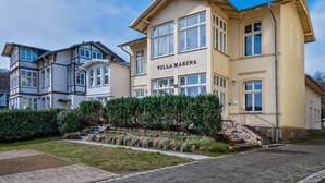 Ein mehrstöckiges Hotel mit auffälligem 'VILLA MARINA'-Schild, einer Steintreppe und einem gepflegten Garten.