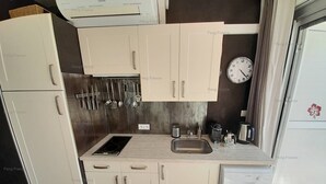 A compact kitchen with white cabinets, a built-in stove, a sink, and a clock on the wall. - Apartment Dune (LE CAP D AGDE)
