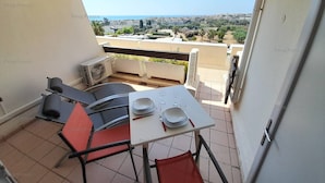 A balcony with a table set for two, chairs, and an air conditioning unit. - Apartment TORNADO (LE CAP D AGDE)