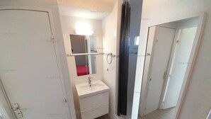 Een kleine badkamer met een witte wasbak, een spiegel, een rode handdoek en een douche.