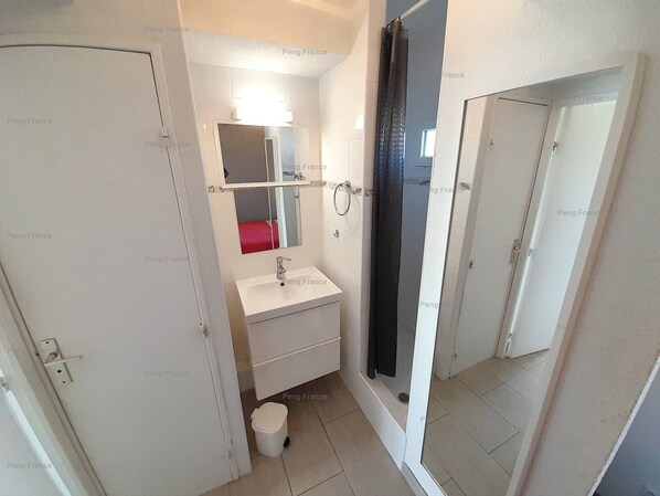 A small bathroom with a white sink, a mirror, a red towel, and a shower area.