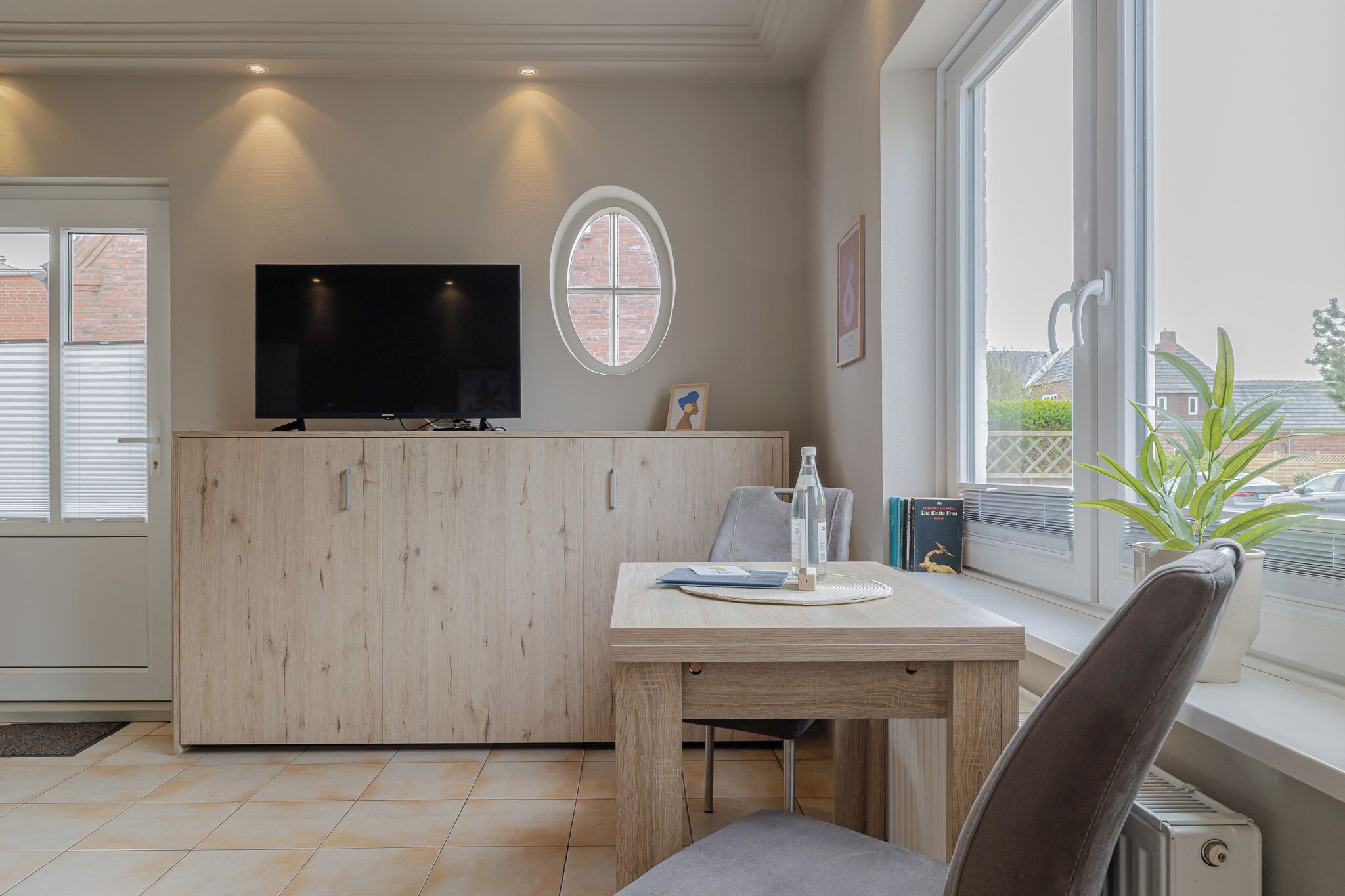 Una camera moderna con una scrivania in legno, una TV a schermo piatto, una pianta in vaso e una finestra con vista sull'esterno.