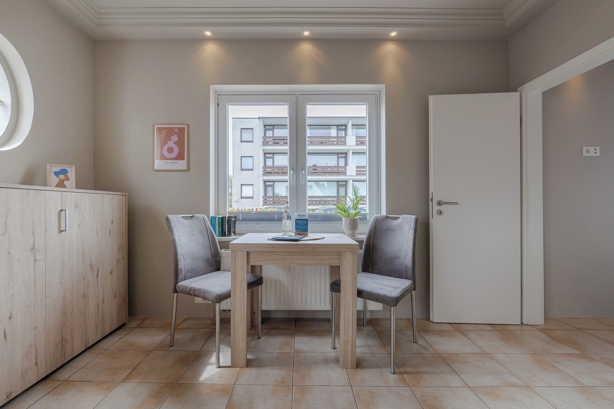 Una cocina moderna con una mesa de comedor, sillas, un armario, una ventana con vistas a edificios y una puerta.