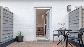 A patio with a table and chairs, a potted plant, and a view into a room with a sofa and a door. - Appartement Seestern (Westerland)