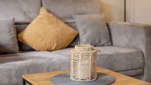 Una cesta de mimbre sobre una mesa de madera con un posavasos gris, ubicada frente a un sofá gris con cojines.