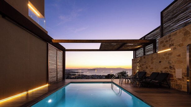 Un espace piscine extérieur moderne avec vue sur la ville au coucher du soleil, une terrasse en bois et des chaises longues.