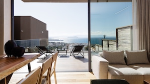 Un balcon avec une table en bois, deux chaises, un canapé et une vue sur la ville et la mer.
