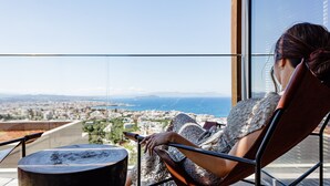Une personne assise sur une chaise de balcon, avec vue sur un paysage urbain et des montagnes.