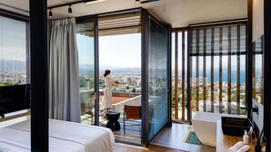 Une chambre moderne dotée d’un grand lit, d’un balcon offrant une vue sur la ville et d’une salle de bain séparée avec une baignoire et un lavabo.