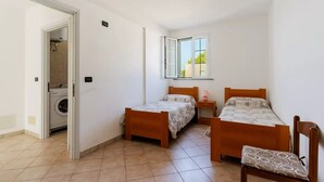 Quarto pequeno e limpo, com duas camas de madeira, uma máquina de lavar roupa e janela com vista para prédios.