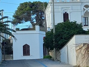 Un vicolo stretto con un edificio bianco, dotato di un piccolo balcone e una finestra con persiana in legno.