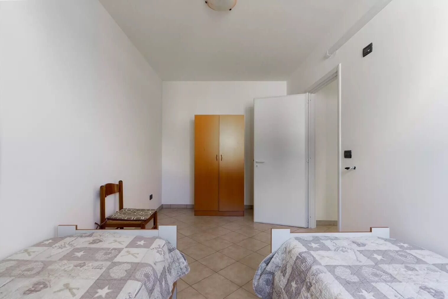 A room with two beds, a chair, a wardrobe, and a door.