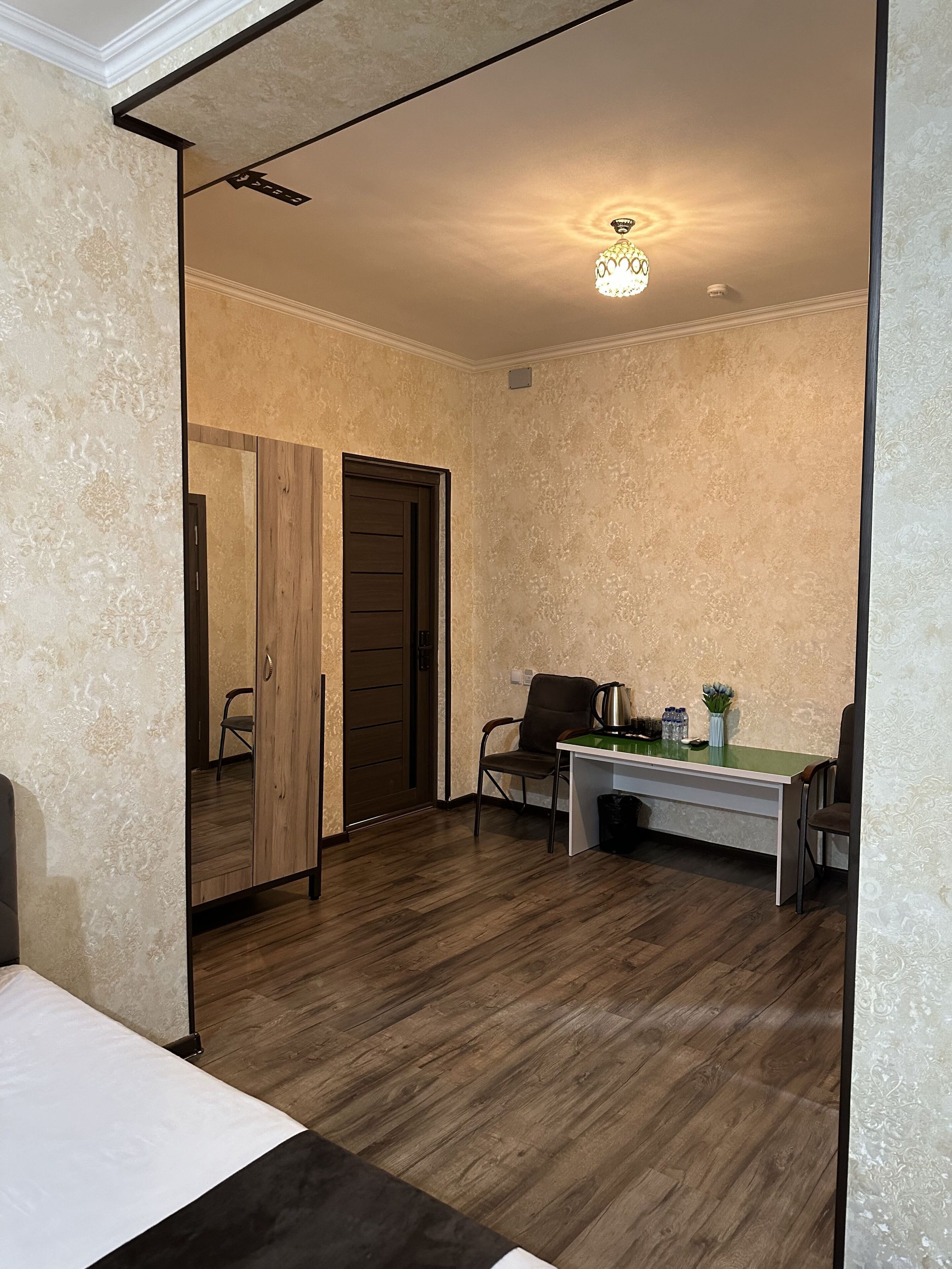 A room with a wooden floor, a desk with a chair, a bed, and a door leading to another room.