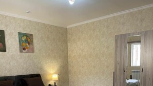 A bedroom with a wooden bed, a nightstand with a lamp, a mirror, and a wardrobe. - Yantai Hotel (Tashkent)