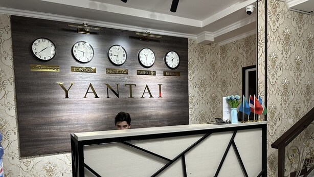 A reception desk with clocks displaying times from New York, London, Moscow, Tashkent, and Beijing. - Yantai Hotel (Tashkent)