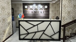 A reception desk with a modern design, featuring a geometric pattern and a wooden backdrop with clocks and city names. - Yantai Hotel (Tashkent)